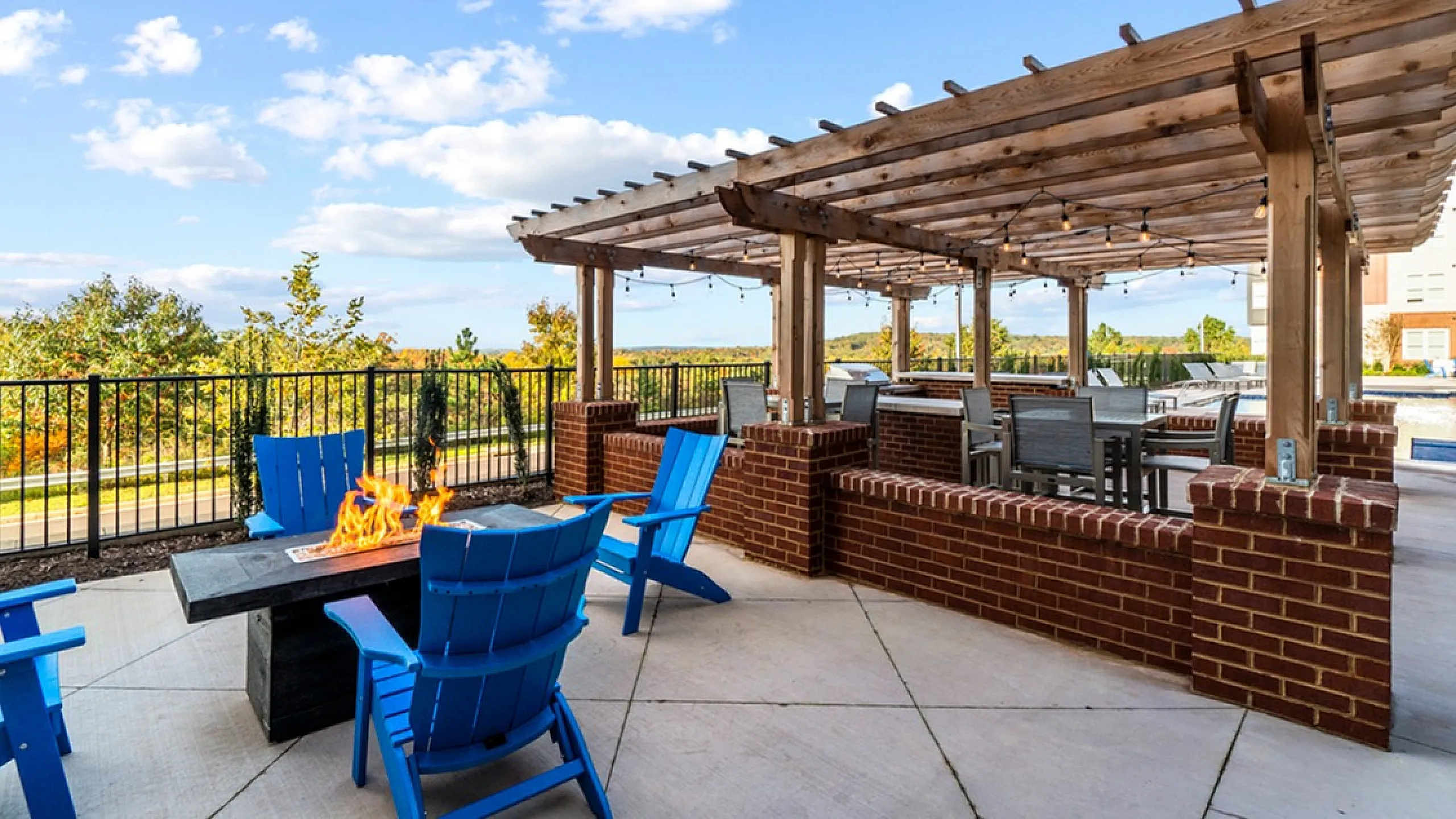 Beautiful outdoor patio with pergola, fire pit, and blue Adirondack chairs at a luxurious apartment complex.