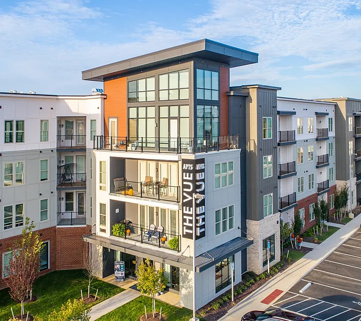 Contemporary apartment complex with expansive balconies and parking area under a clear sky.