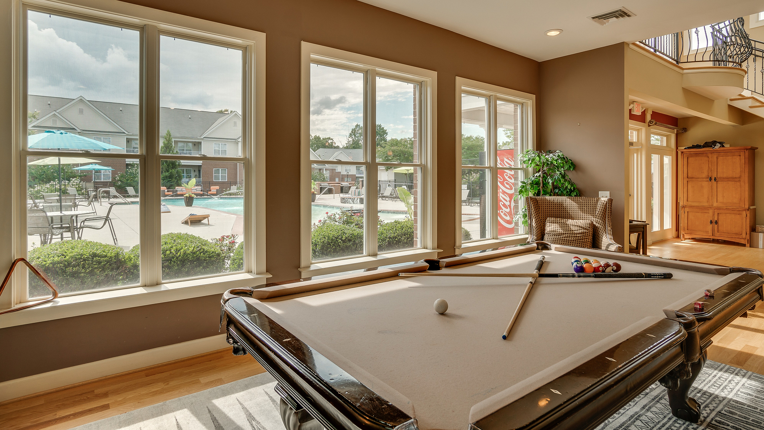 Spacious recreational room featuring a pool table with a view of the sunlit outdoor pool area.