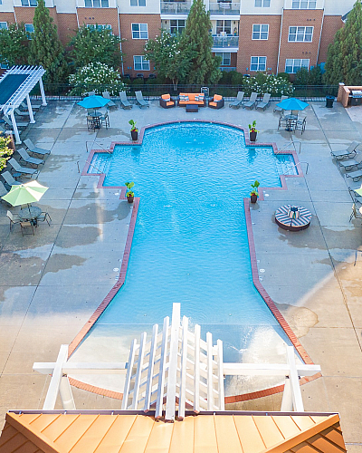 Aerial view of a stylish apartment complex pool with lounge chairs and colorful umbrellas.