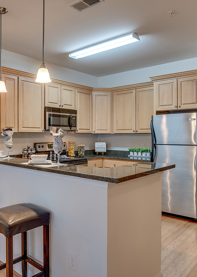 Modern kitchen with light wood cabinets, stainless steel appliances, and a stylish breakfast bar with pendant lighting.