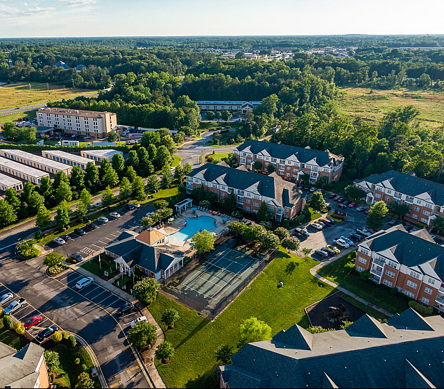 Aerial view of a vibrant residential community featuring modern apartments, a central swimming pool, and lush green surroundings.