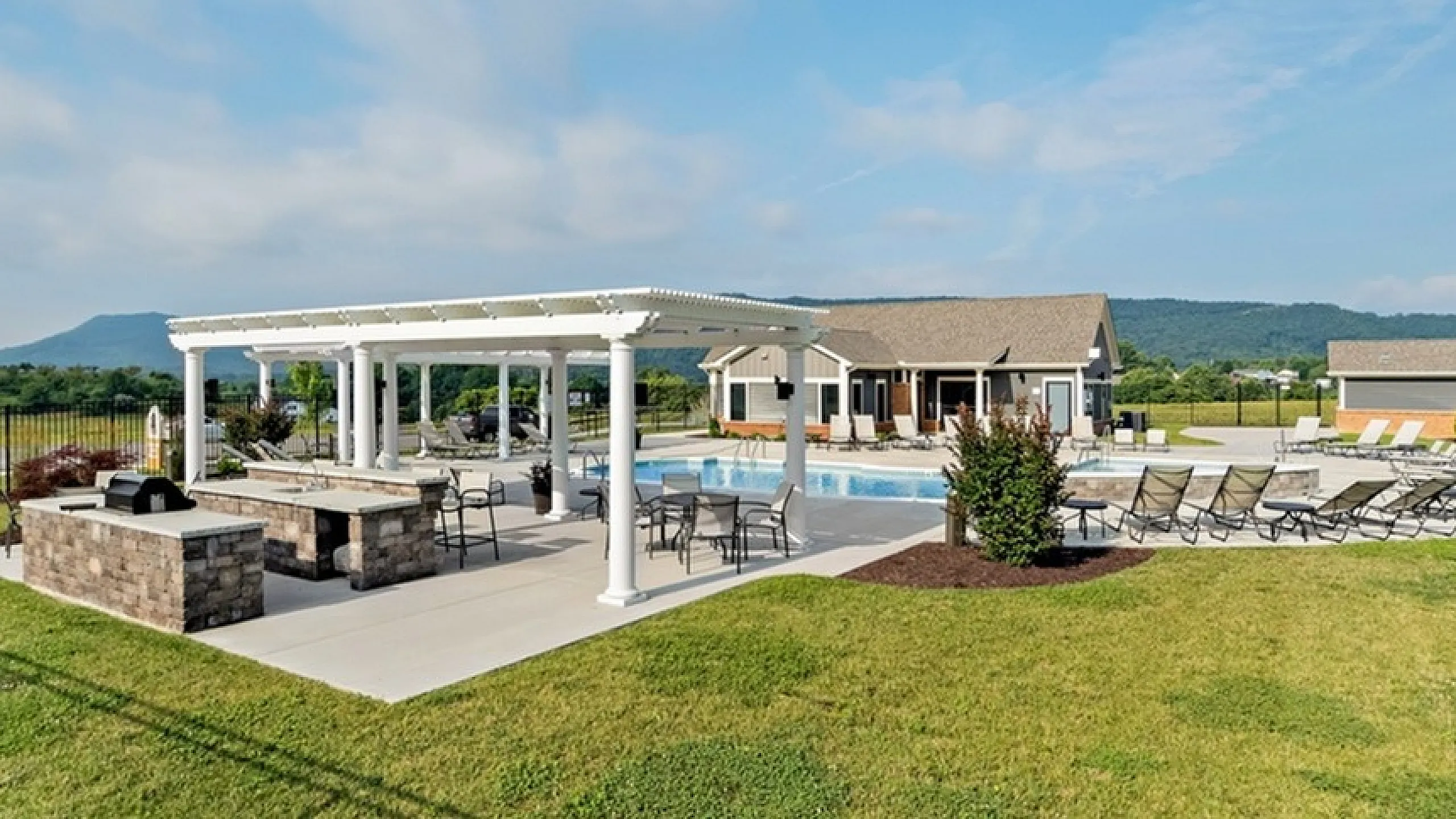 Inviting outdoor area with a pergola, modern grill station, and sparkling swimming pool against a mountain backdrop.