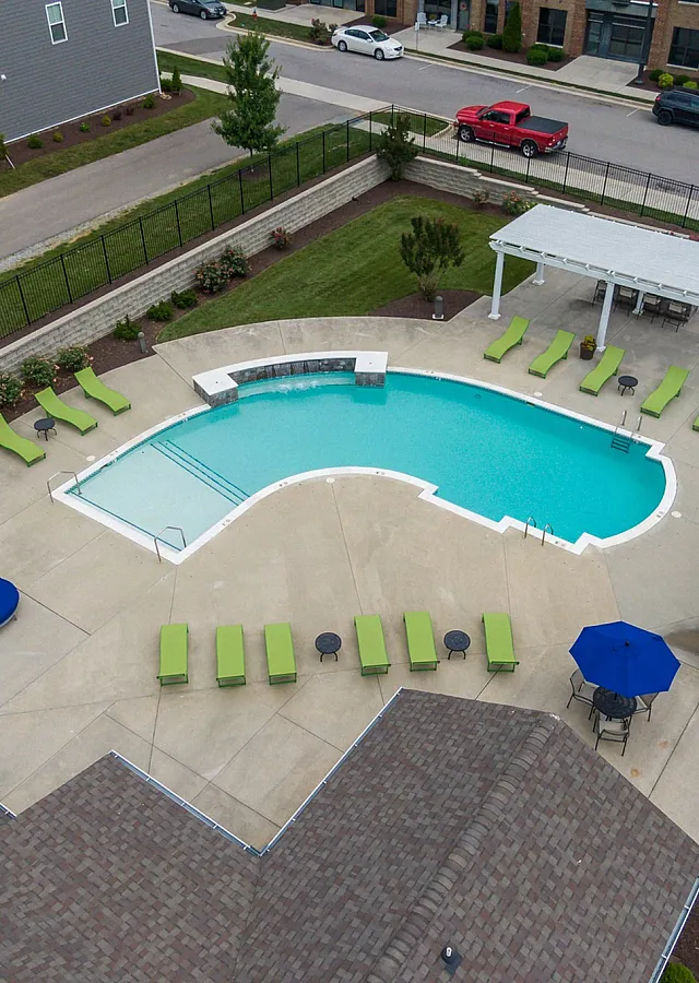 Aerial view of a chic outdoor pool surrounded by green lounge chairs and blue umbrellas.