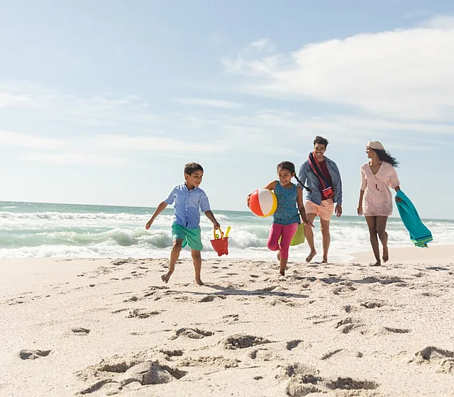 Happy family enjoying a sunny day at the beach, children playing with a beach ball and bucket.