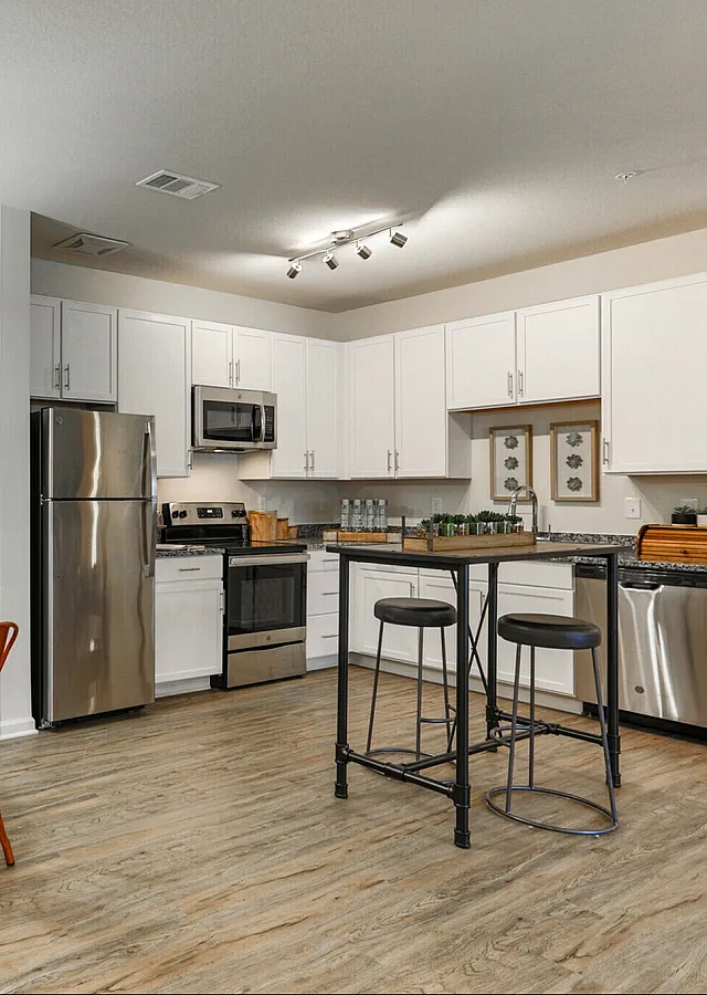 Modern kitchen with stainless steel appliances, cozy dining nook with orange chairs, and elegant lighting.