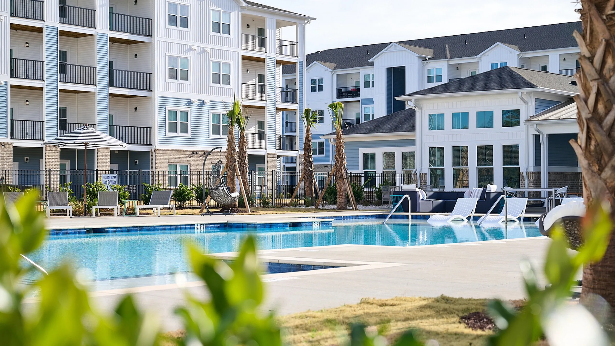 Elegant apartment complex with a sparkling pool, surrounded by lush greenery and modern architecture.