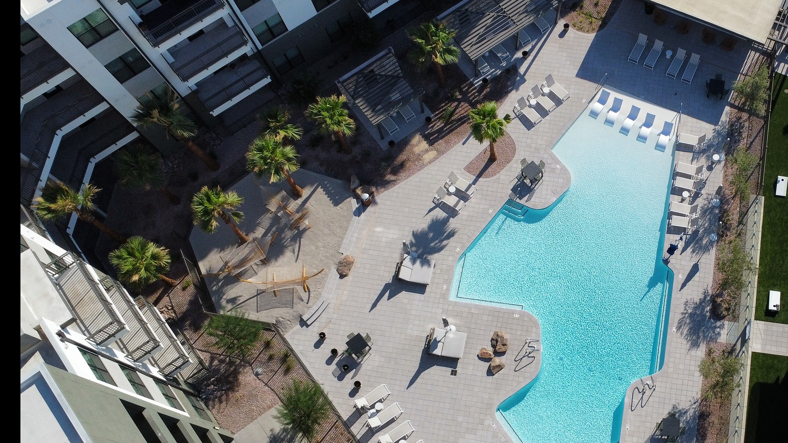 Aerial view of a luxurious swimming pool surrounded by modern apartment buildings and lush palm trees.