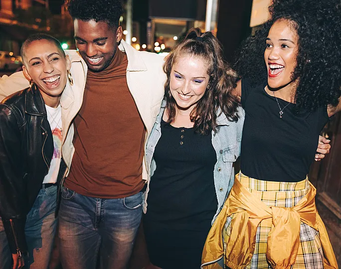 four people walking and smiling on sidewalk at night