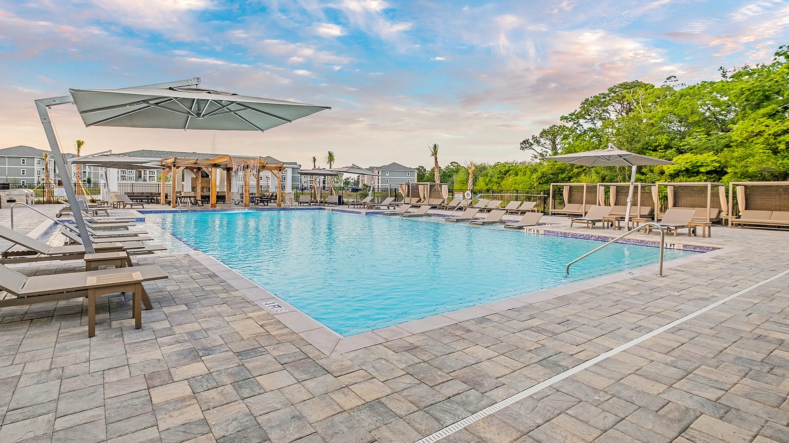 Luxurious apartment complex pool area with elegant lounge chairs, modern cabanas, and expansive blue skies.