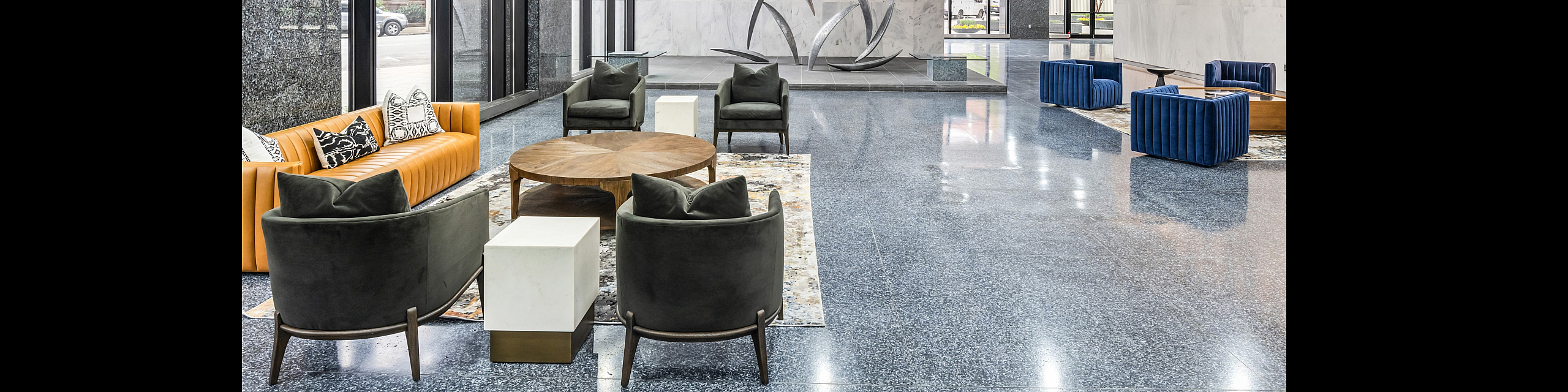 Elegant apartment lobby with modern decor, featuring plush seating and unique wall art under natural light from floor-to-ceiling windows.