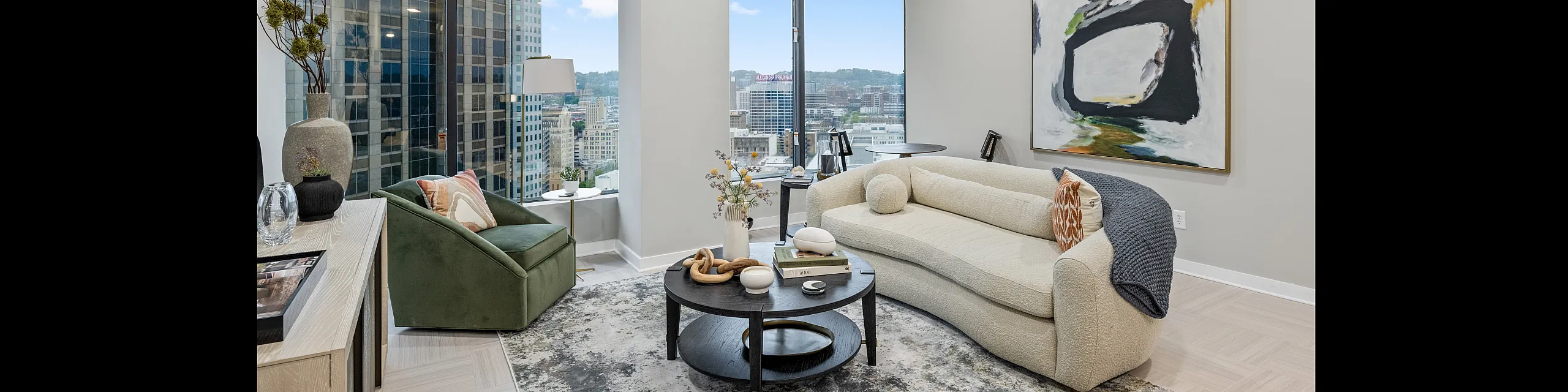 Elegant high-rise apartment living room with floor-to-ceiling windows offering a panoramic city skyline view, plush furnishings, and modern art.