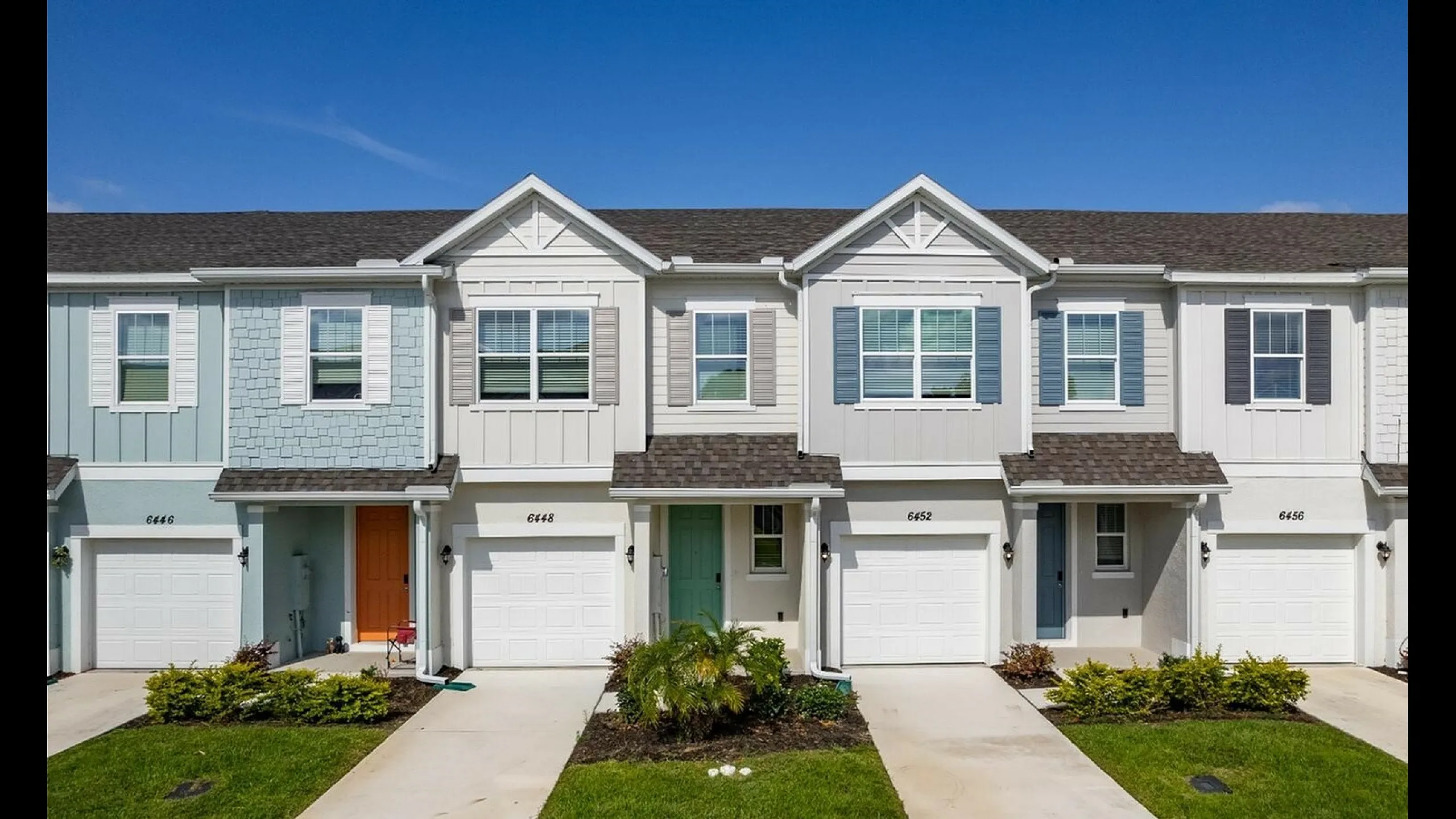 Charming townhouses with stylish fa&ccedil;ades, featuring colorful doors and manicured lawns under a clear blue sky.