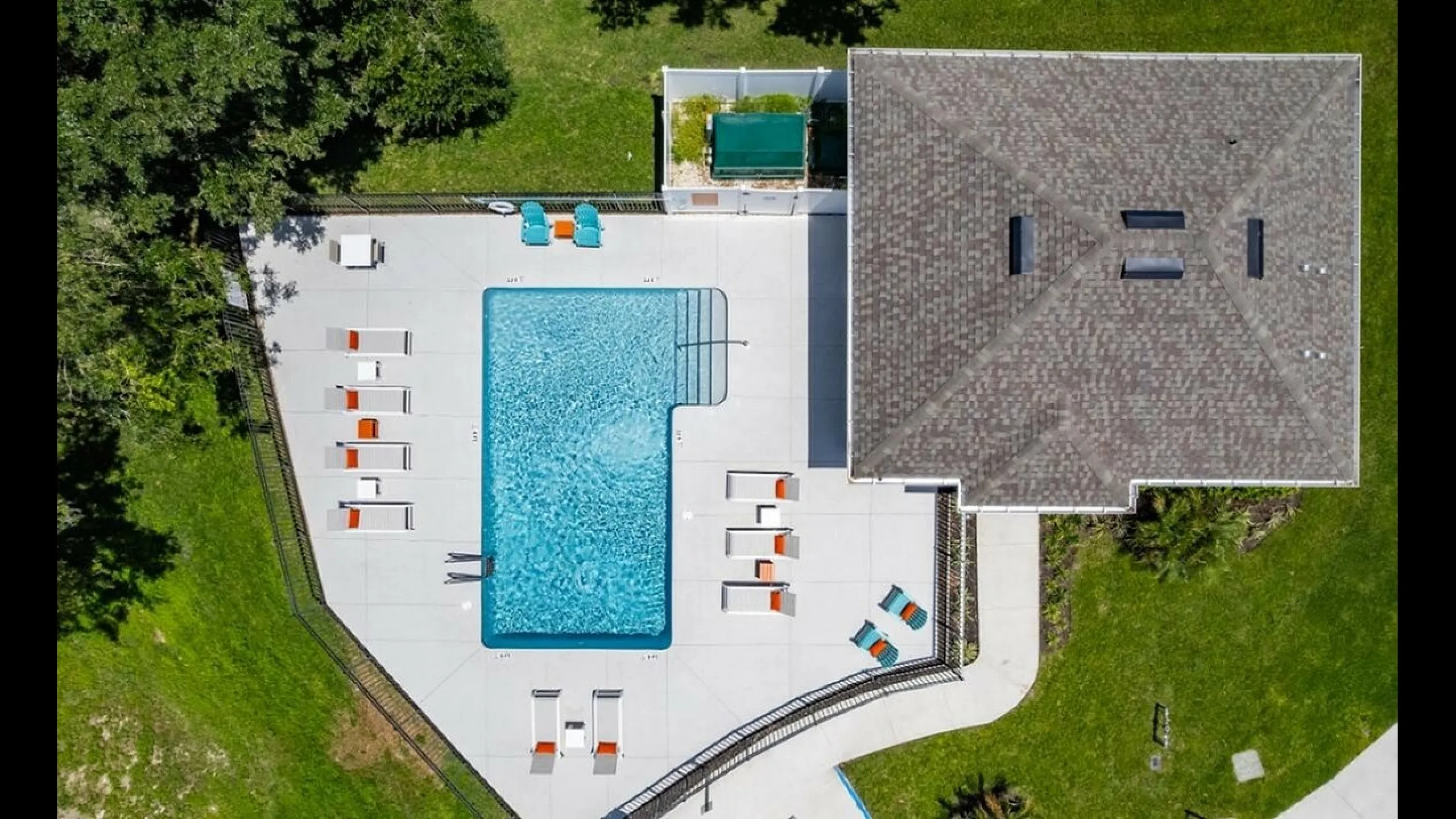 Aerial view of a luxurious apartment complex pool area with modern sun loungers, vibrant landscaping, and a spacious deck for relaxation.