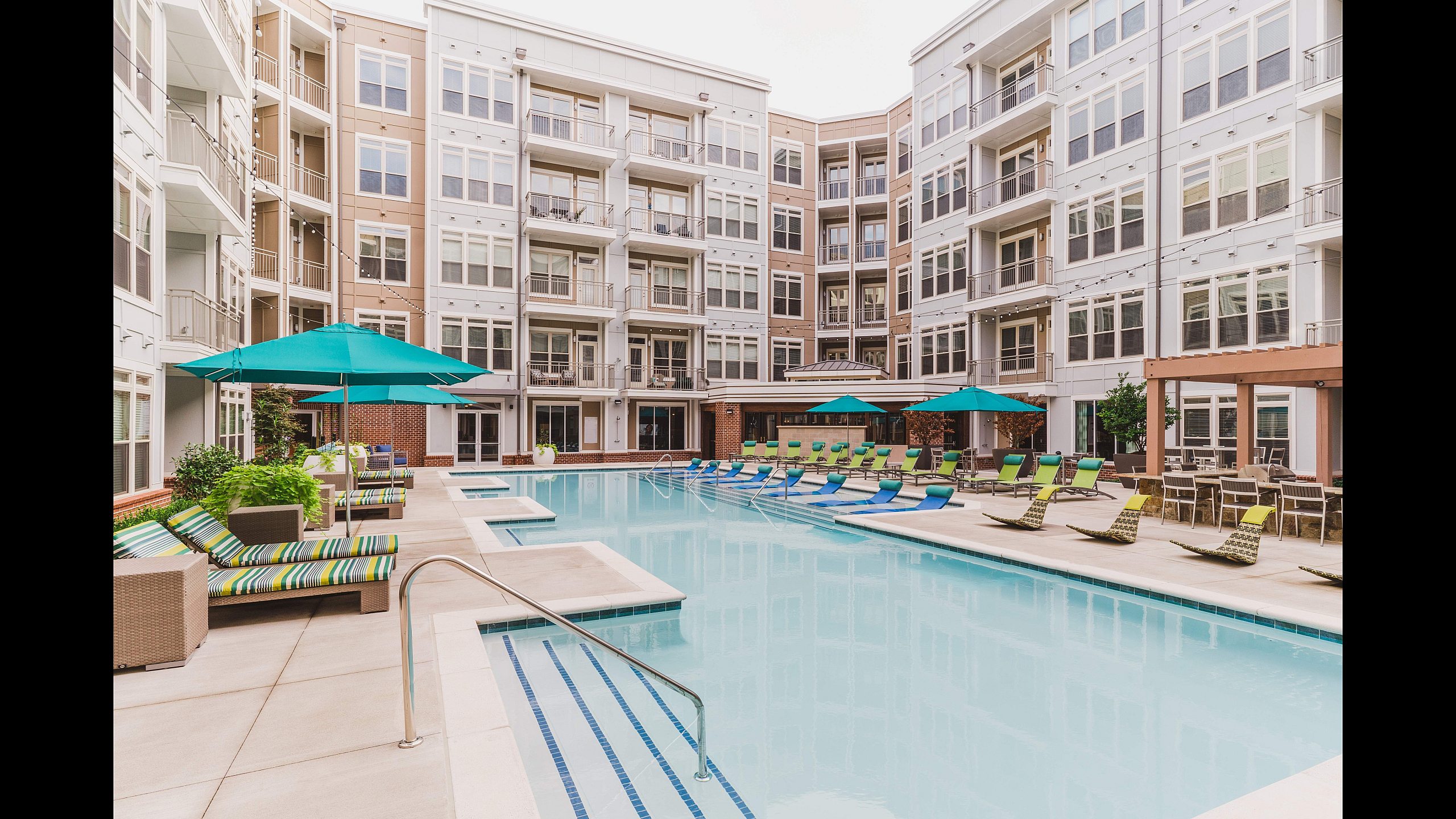 Luxurious apartment complex with a sparkling outdoor pool, stylish lounging area, and sleek modern architecture, perfect for relaxation and comfort.