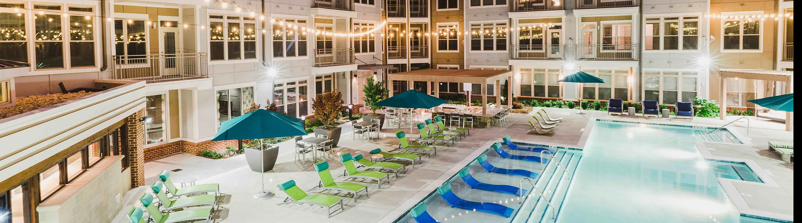 Luxurious apartment complex at night with a beautifully lit outdoor pool, stylish lounge chairs, and inviting ambiance.