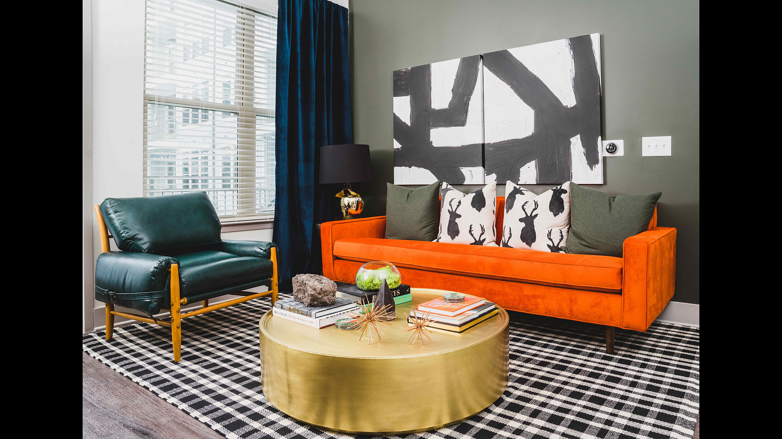 Chic modern living room with vibrant orange sofa, stylish artwork, and elegant gold coffee table on checkered rug.