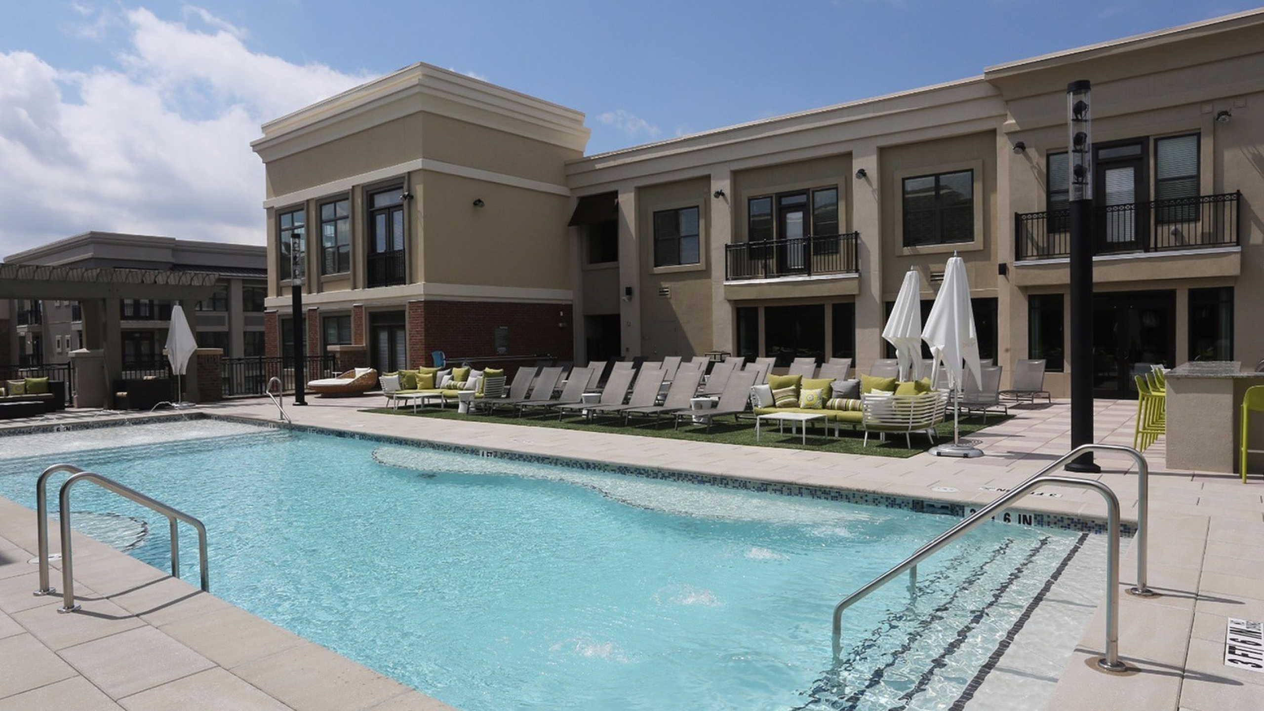 Luxurious apartment complex featuring a pristine outdoor pool, surrounded by comfortable loungers and stylish outdoor seating.