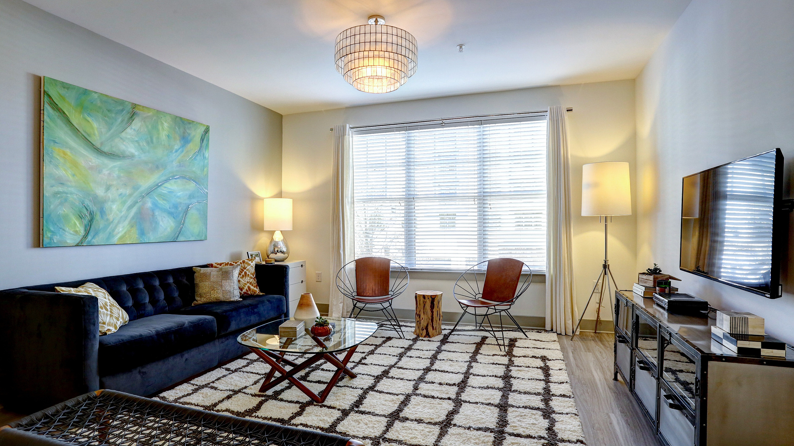 Bright and inviting living room with contemporary decor, featuring a plush navy sofa, abstract wall art, large window with natural light, and stylish lighting fixtures.
