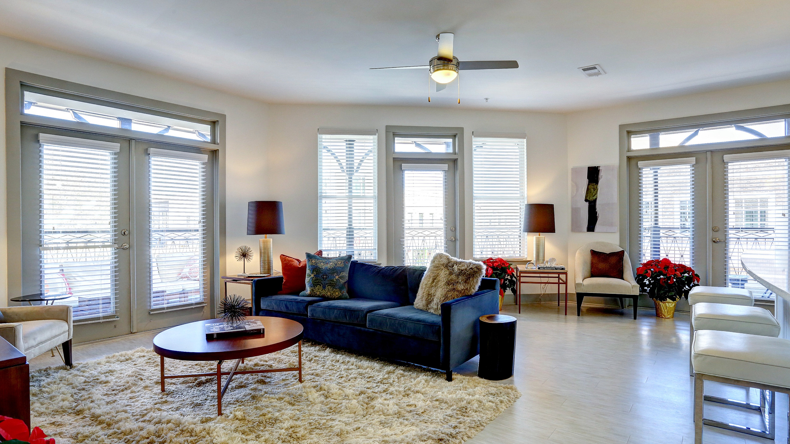 Modern living room with plush navy sofa, chic coffee table, and elegant lighting surrounded by floor-to-ceiling windows with ample natural light.