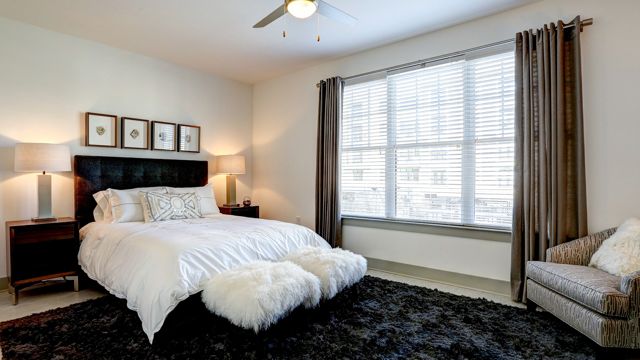 Elegant bedroom with luxurious decor, featuring a plush bed, stylish nightstands, chic artwork, and a cozy seating area by a large window.