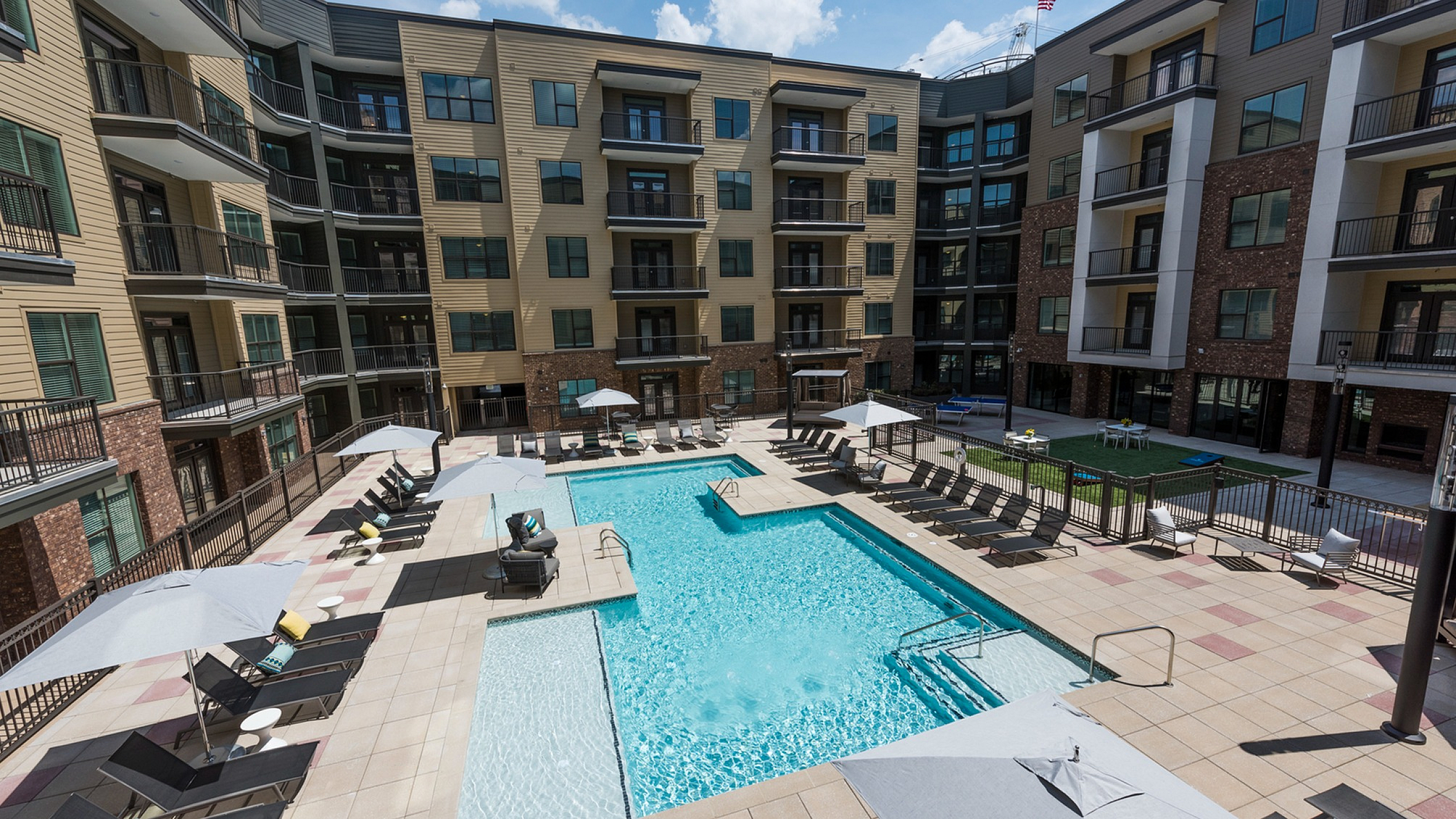Luxurious apartment complex featuring a sparkling pool, sun loungers, and modern architecture with spacious balconies.
