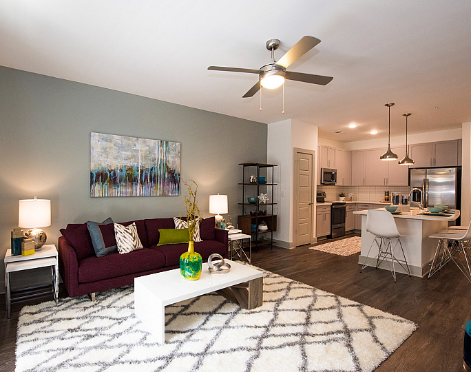 Modern, open-concept living room with stylish decor, cozy sofa, vibrant curtains, and a chic kitchen with elegant lighting.
