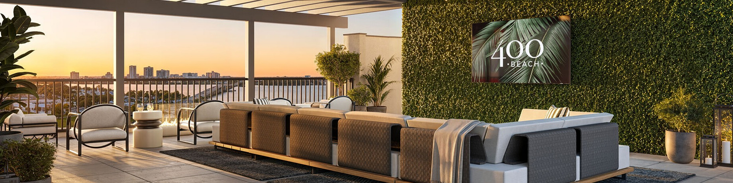 Elegant rooftop lounge with stylish seating, lush green wall, and string lights creating a cozy ambiance against a sunset backdrop.