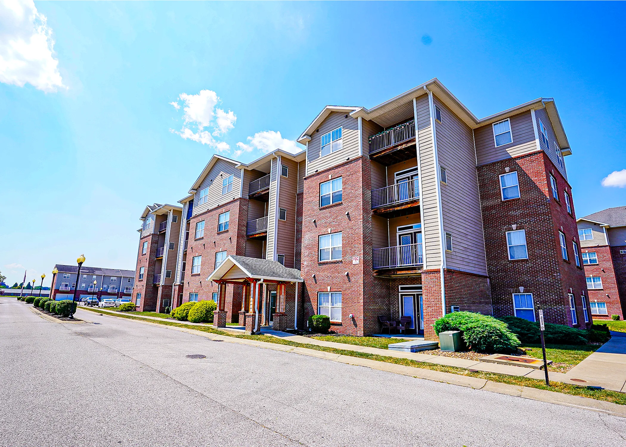 Charming brick apartment complex with modern balconies and lush landscaping under a clear blue sky.