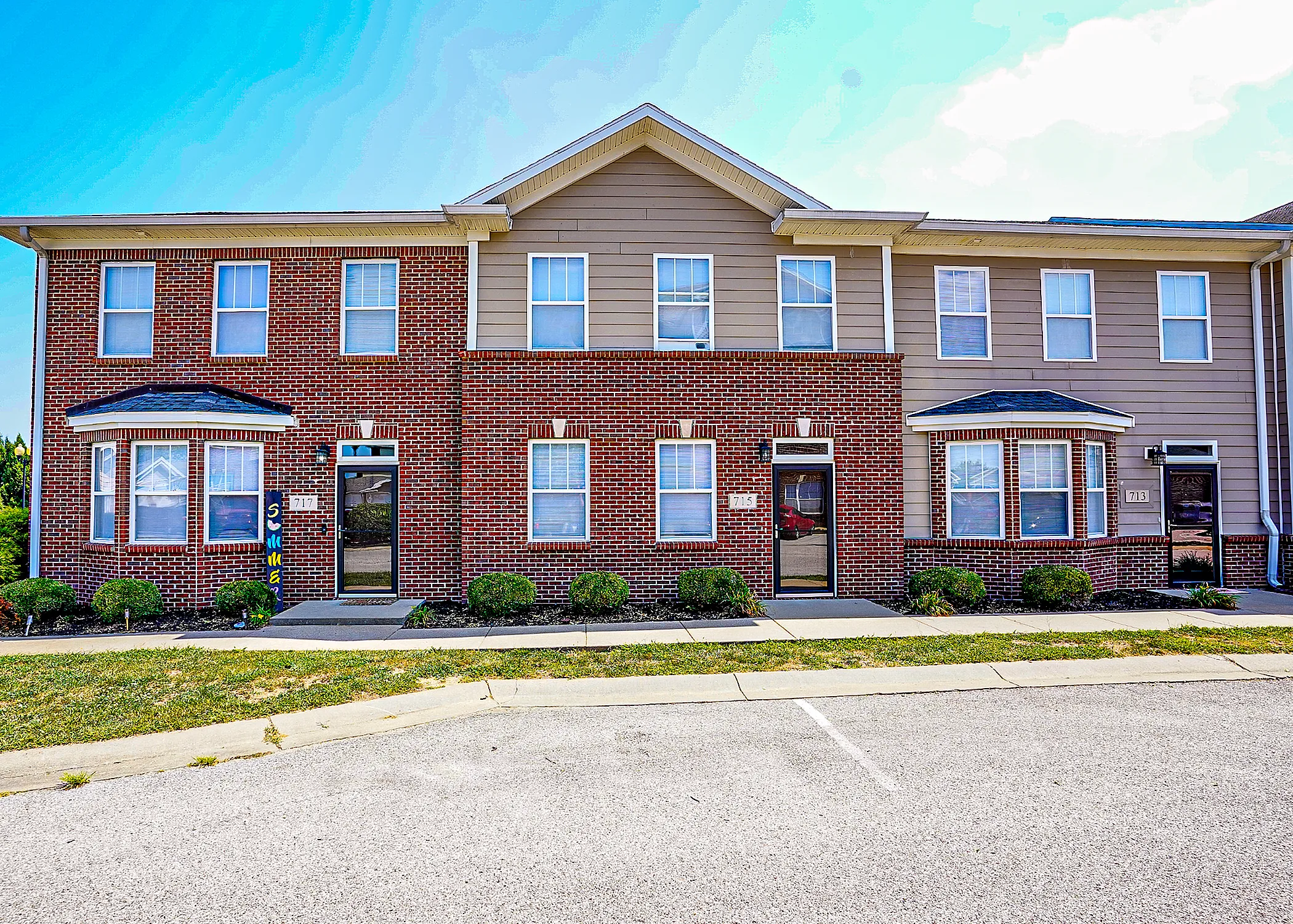 Charming townhouse complex with beautiful brick facade, featuring large windows and manicured landscaping under a clear blue sky.
