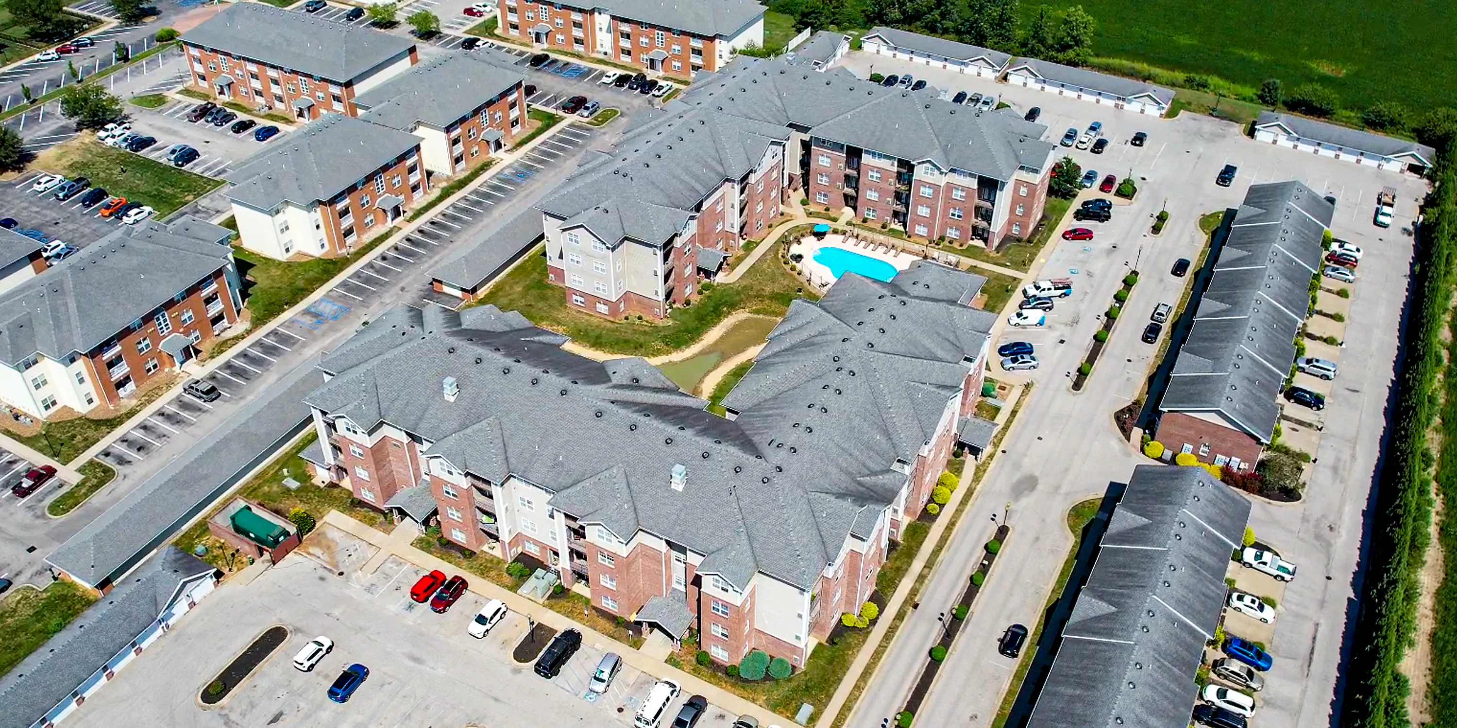 Aerial view of a modern apartment complex with spacious parking, green spaces, and a vibrant swimming pool, offering an ideal residential experience.