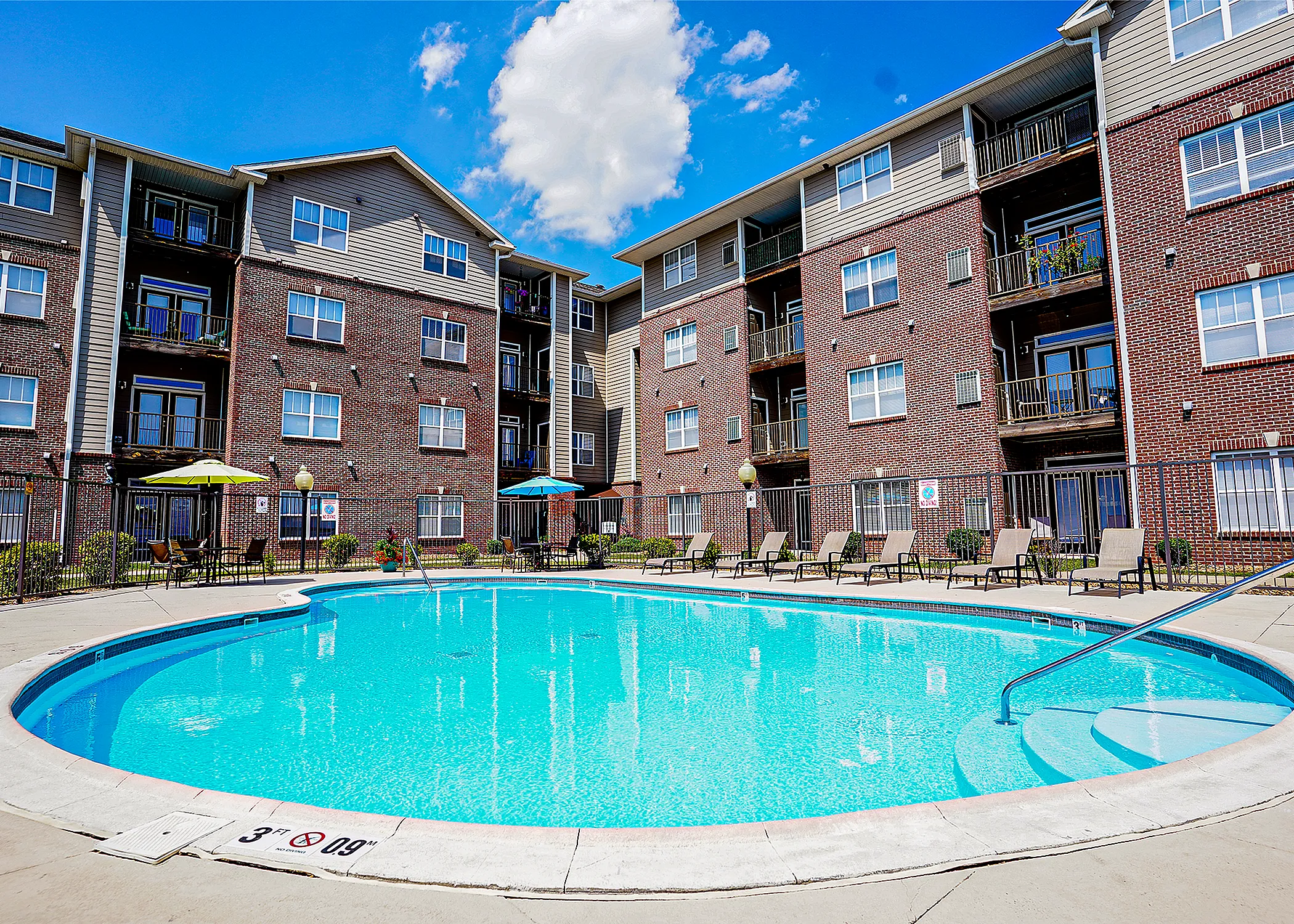 Charming apartment complex with a sparkling outdoor pool, surrounded by stylish lounge chairs and colorful umbrellas, perfect for relaxation and entertaining.