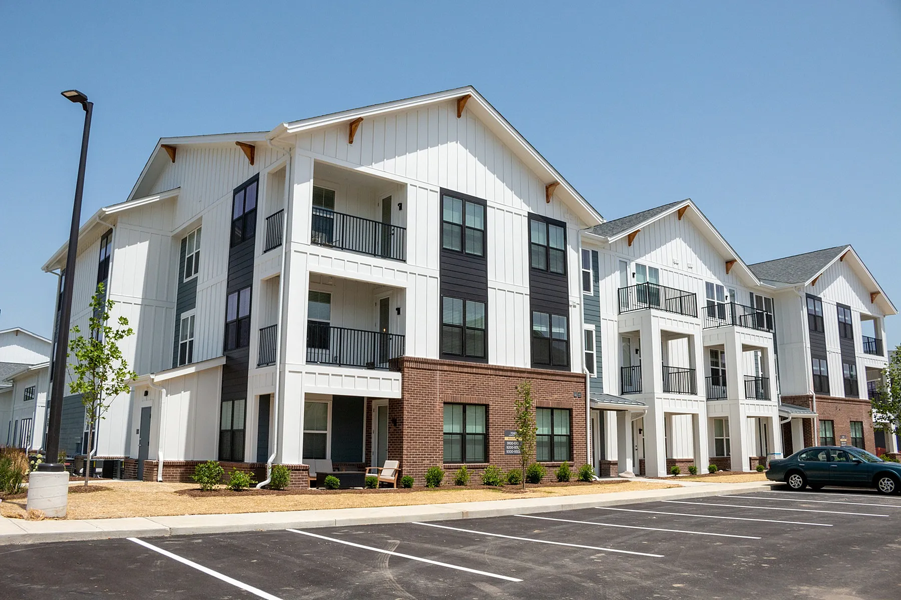 Modern apartment complex with stylish balconies, ample parking, and fresh landscaping under a clear blue sky.