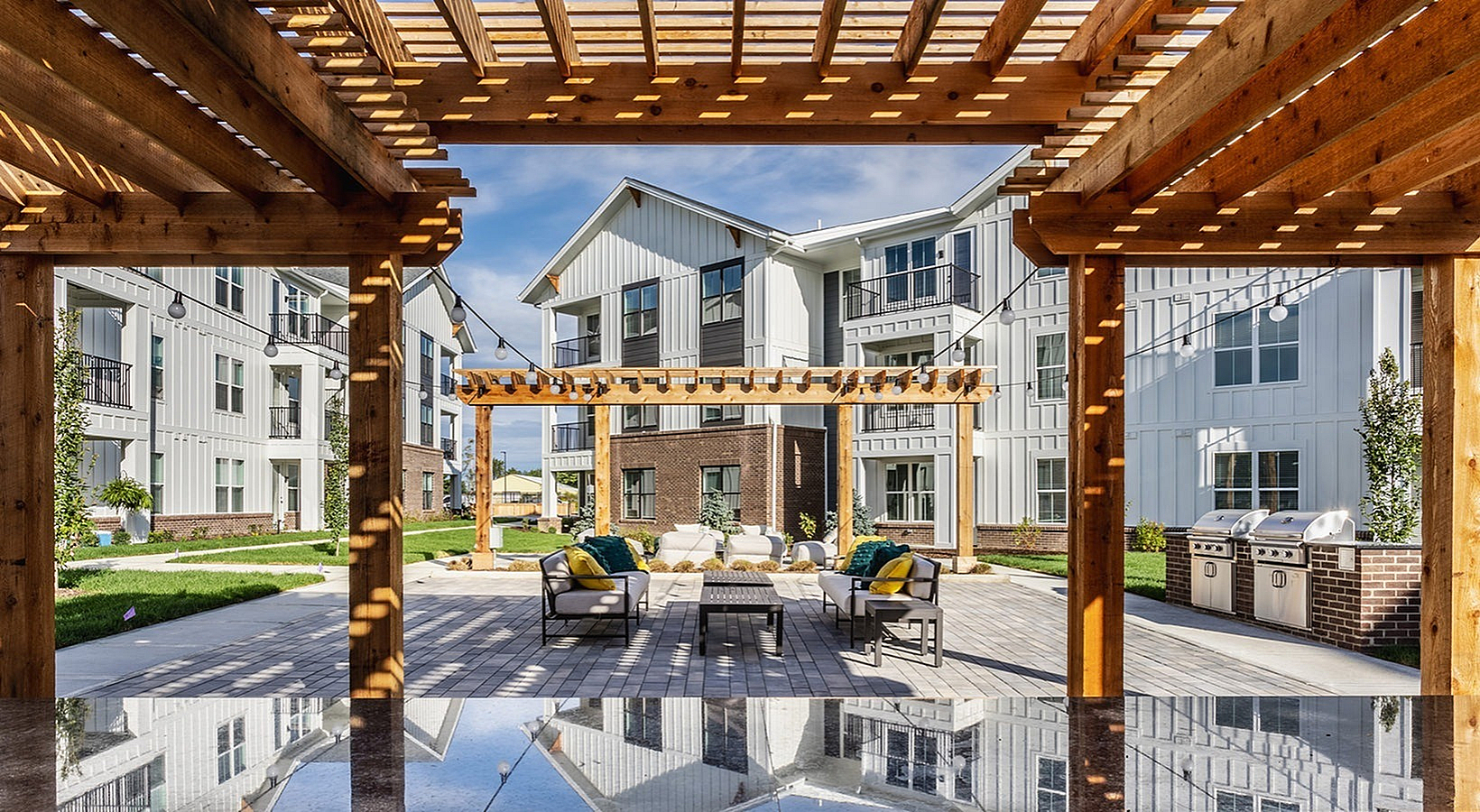 Charming outdoor community patio with stylish pergola, modern seating area, and barbecue grills, set against a backdrop of elegant apartment buildings.