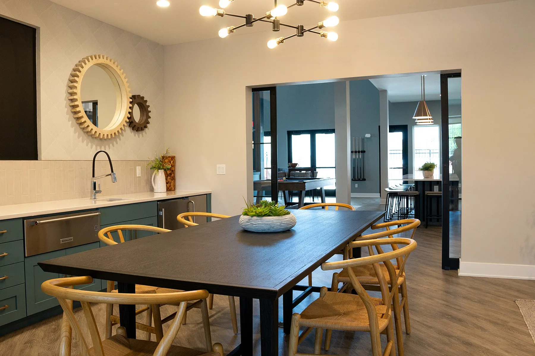 Contemporary dining area with sleek dark table, stylish wooden chairs, modern chandelier, and open kitchen layout.