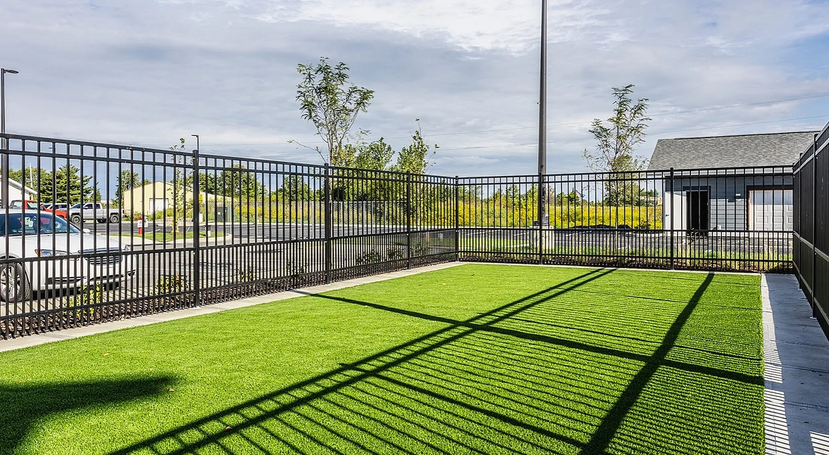 Charming outdoor area with lush green artificial turf, enclosed by an elegant black metal fence, ideal for relaxation and leisure activities.