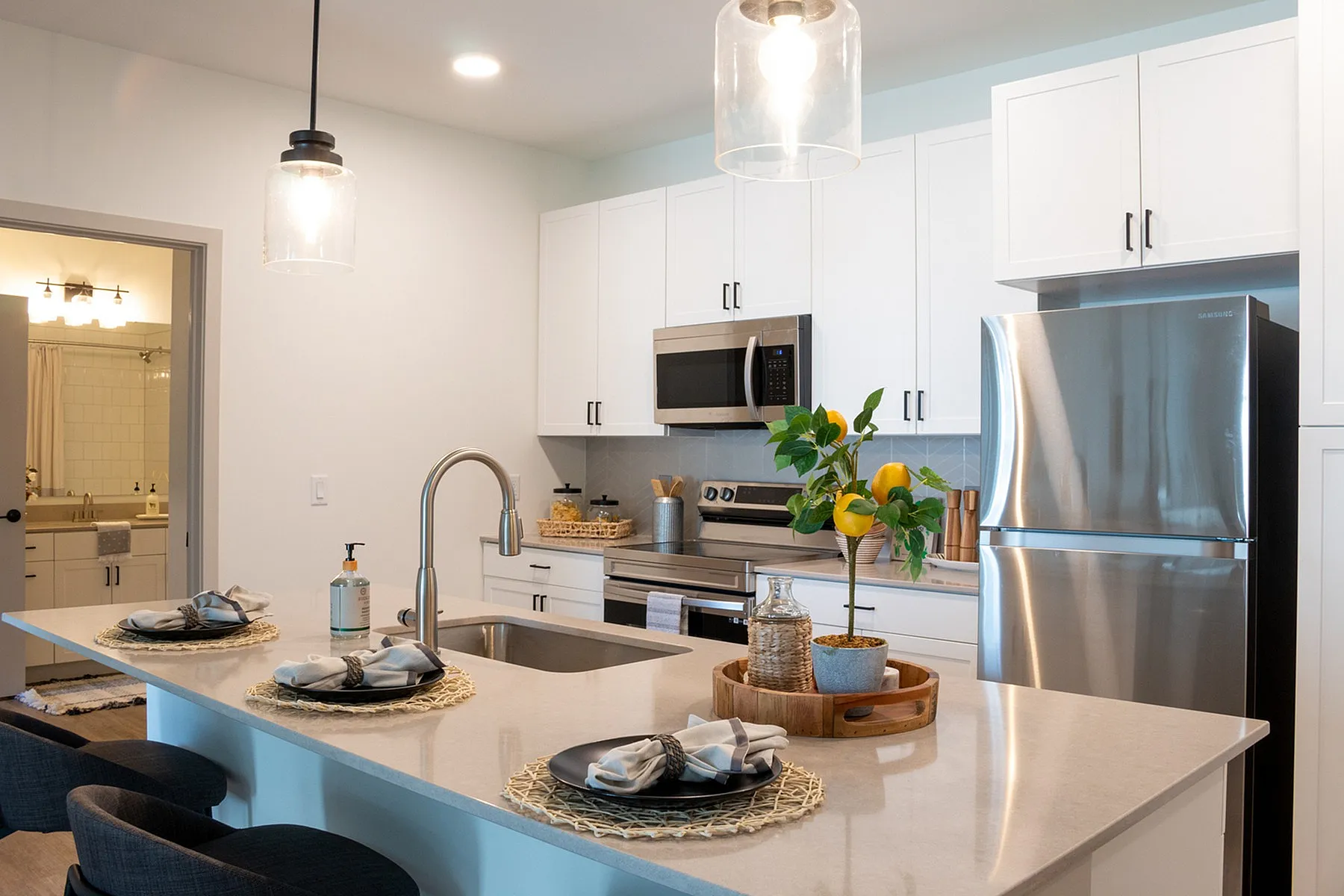 Modern kitchen with sleek white cabinetry, stainless steel appliances, and a chic island featuring elegant bar stools and stylish pendant lighting.