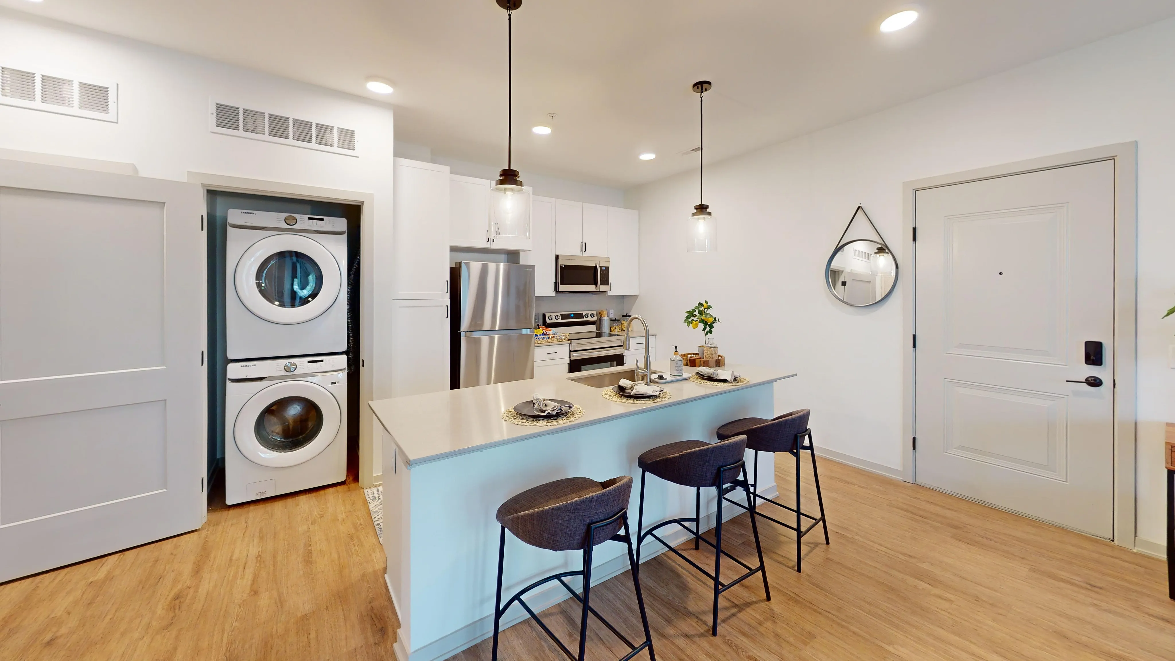 Modern kitchen featuring a sleek island with bar stools, pendant lighting, and convenient in-unit laundry appliances.