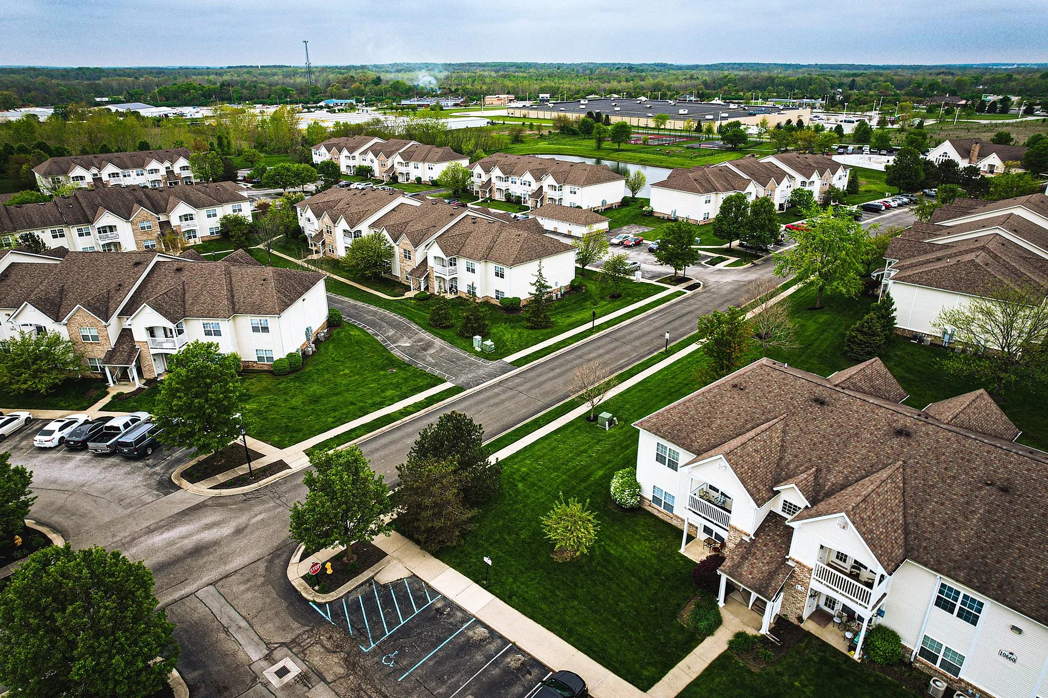 Charming aerial view of a serene residential neighborhood, showcasing elegant white two-story townhouses with lush green lawns and scenic landscaping.