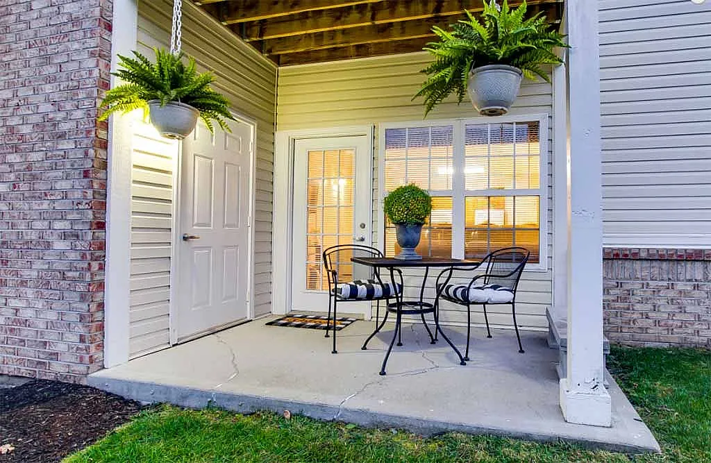 Charming apartment patio featuring elegant outdoor seating, lush hanging ferns, and cozy ambiance.