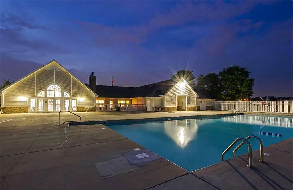 Inviting outdoor pool area with charming clubhouse, beautifully lit at dusk, offering a perfect relaxation spot for residents.