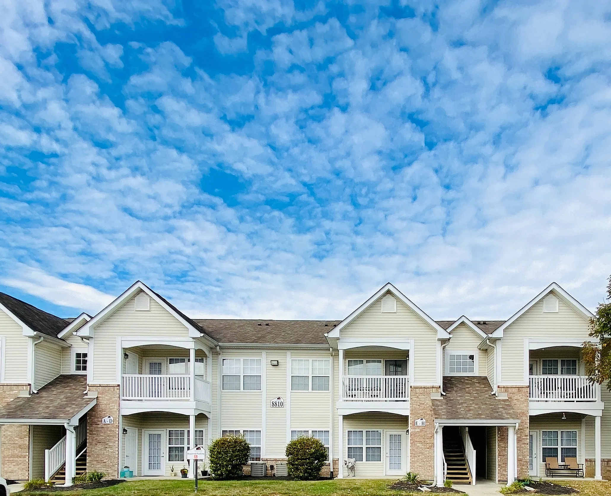 Charming apartment building with inviting white exteriors, balconies, and well-maintained landscaping under a clear blue sky.