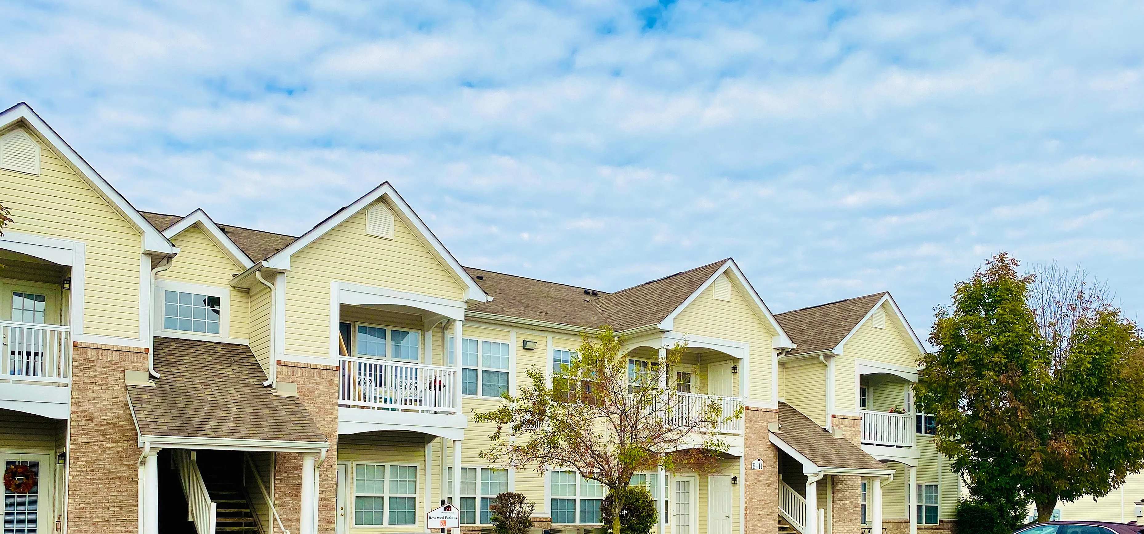 Charming two-story apartment complex with inviting balconies, surrounded by lush greenery and a bright clear sky.
