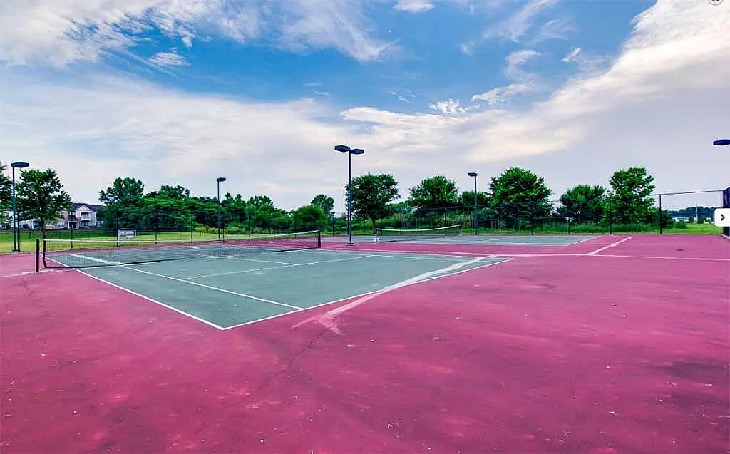 Vibrant tennis court surrounded by lush greenery and clear blue skies, perfect for outdoor sports enthusiasts.