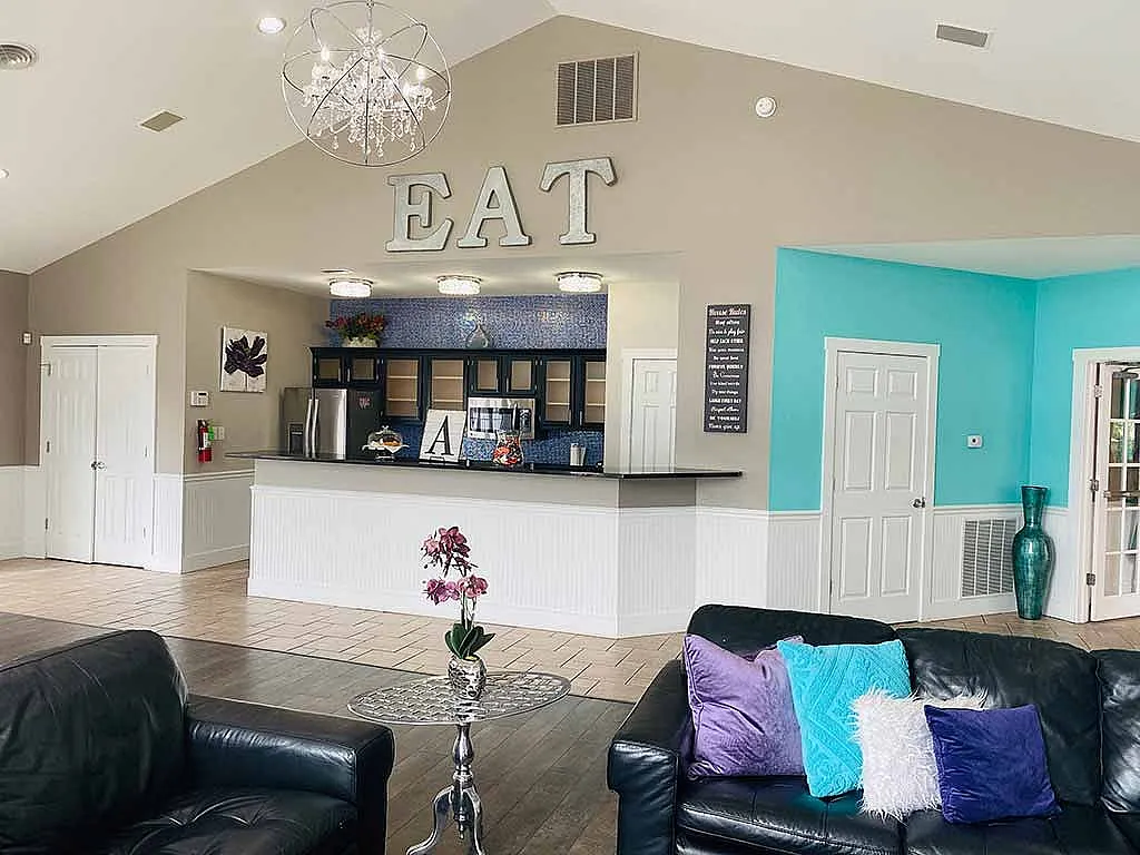 Inviting common area with stylish decor, featuring cozy black leather seating, vibrant pillows, and a modern kitchen with stainless steel appliances.