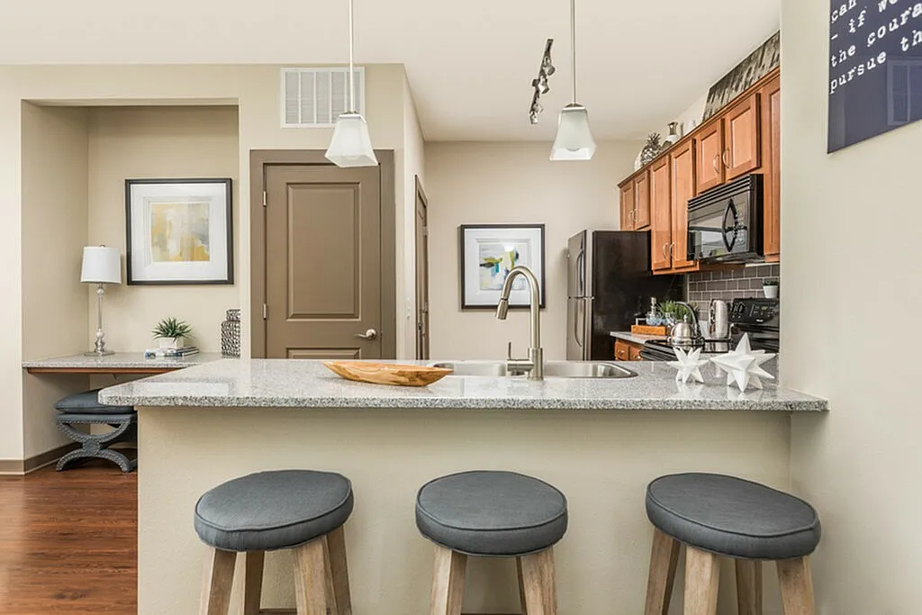Modern kitchen with granite countertop, sleek bar stools, and stylish wood cabinetry, offering a perfect blend of functionality and elegance.