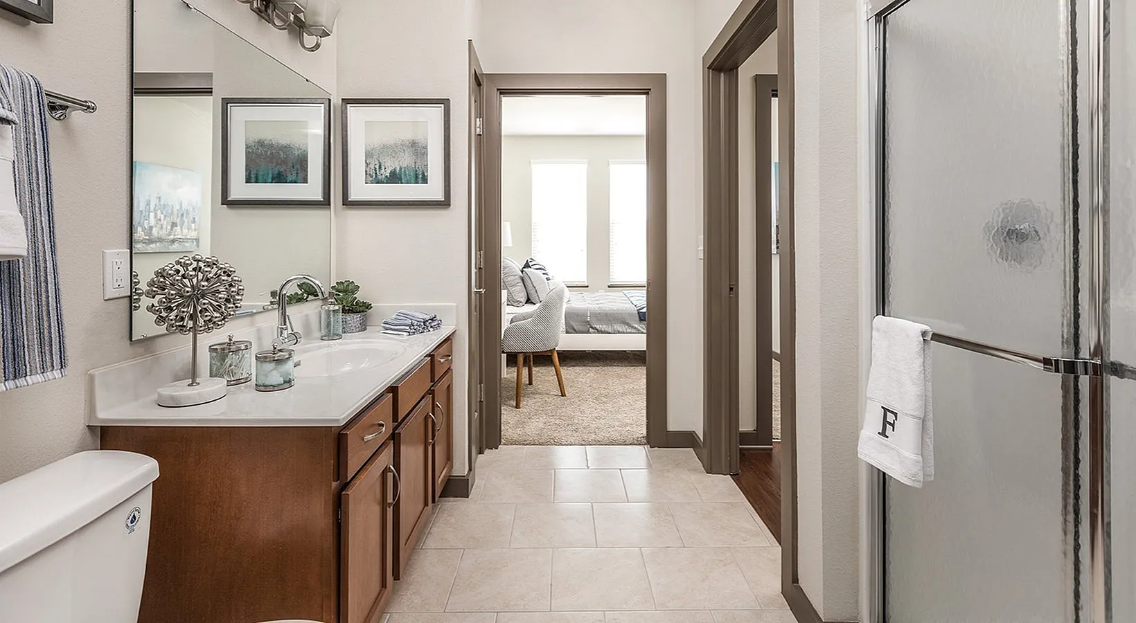 Elegant bathroom with chic decor, leading to a cozy bedroom with abundant natural light, highlighting modern apartment living.