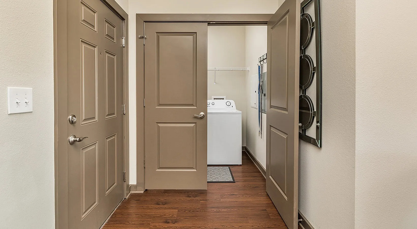 Inviting apartment hallway with elegant wooden flooring leading to a convenient laundry room with modern appliances.