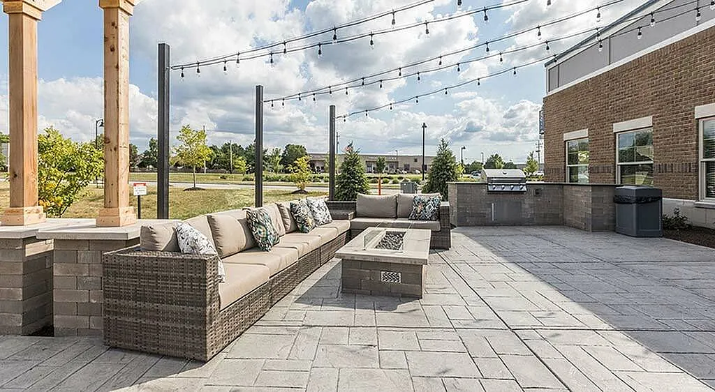 Charming outdoor patio featuring comfortable wicker seating, elegant fire pit, string lighting, and a built-in grill, perfect for entertaining.