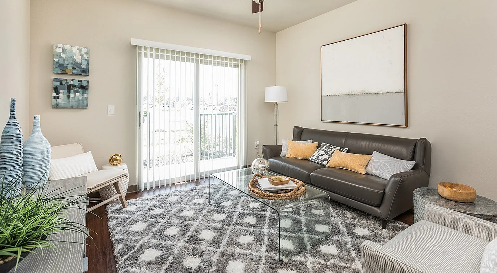 Modern living room with a sleek gray leather sofa, abstract art on walls, and floor-to-ceiling window offering ample natural light.